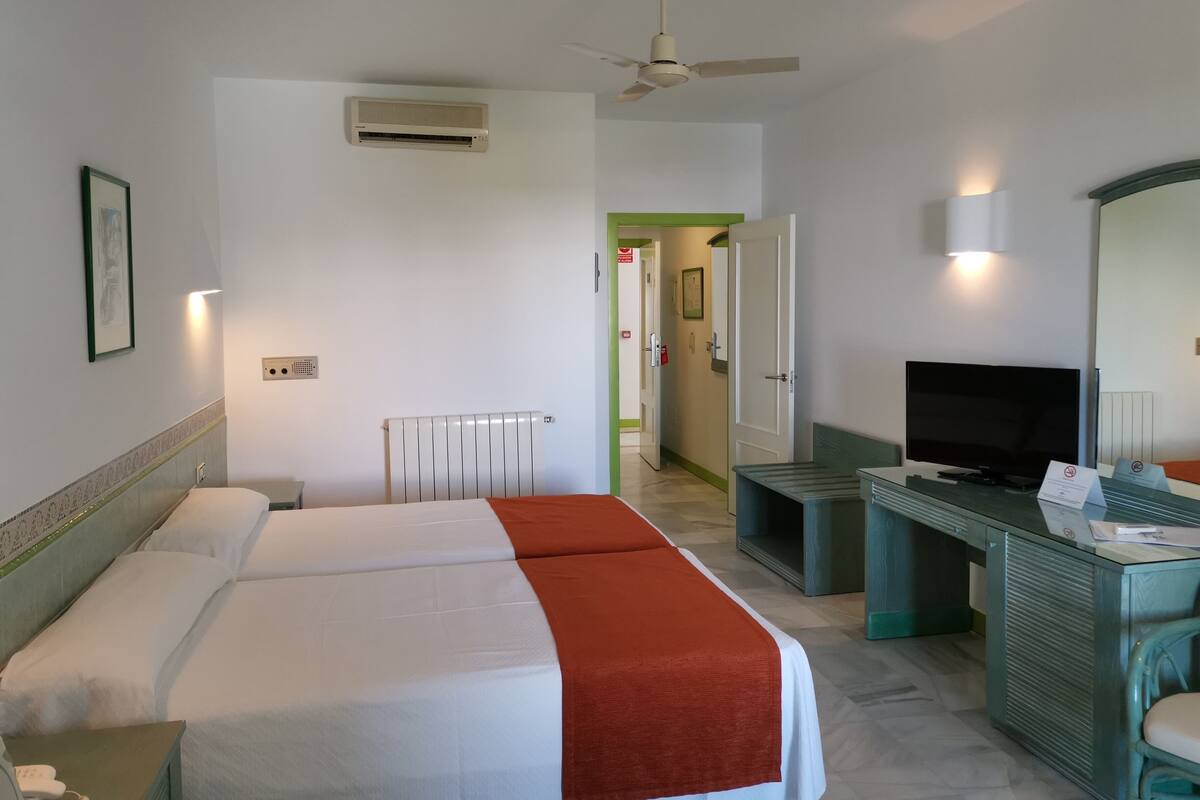 Une chambre d’hôtel comprenant un lit, un bureau avec une télévision, un miroir et un ventilateur de plafond.
