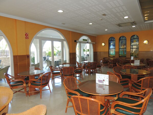 A spacious indoor dining area with wicker chairs and tables, large windows, and a view of the outdoor patio.