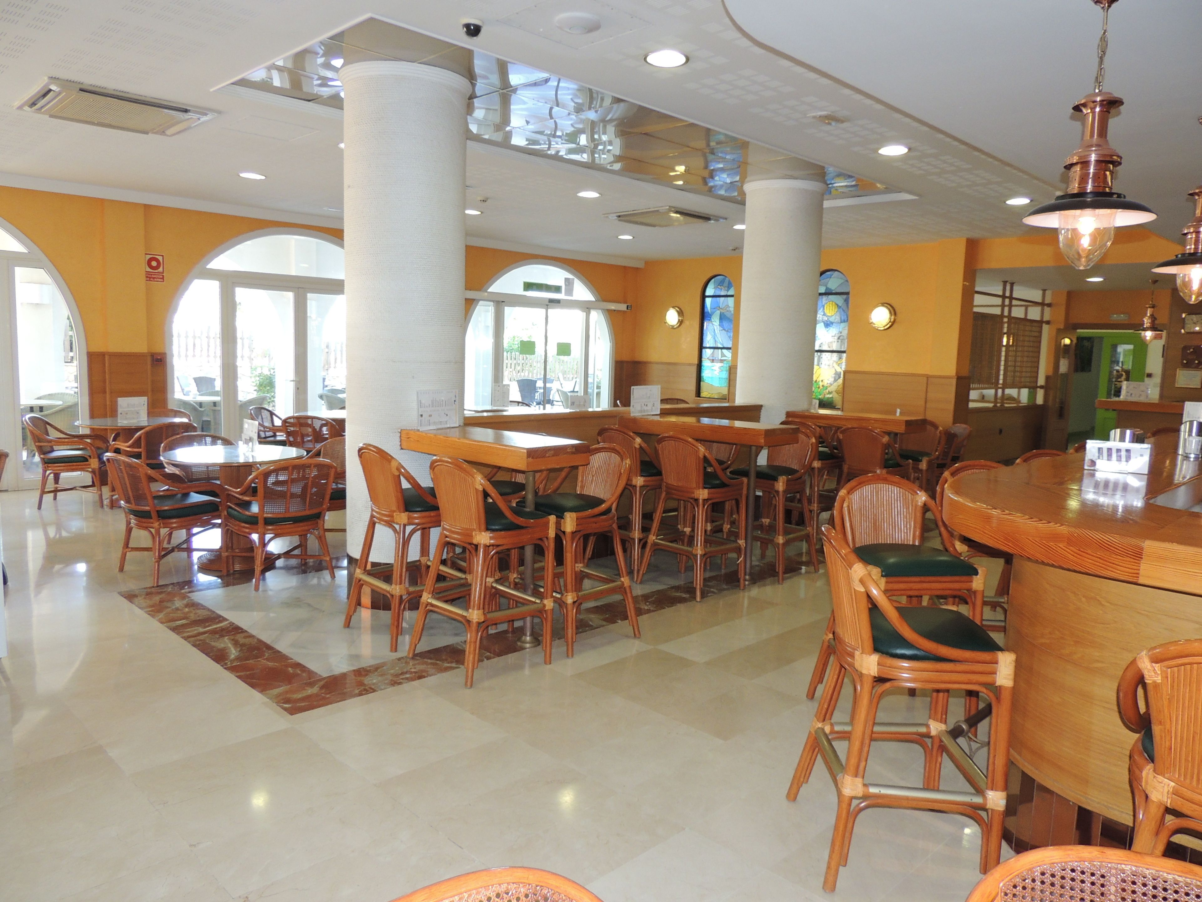A spacious restaurant with high ceilings, large windows, and a variety of seating arrangements including round tables and individual chairs.