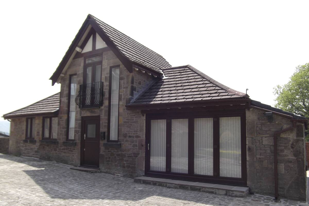 A stone building with a pitched roof, large windows, and a door.