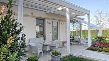 Un patio techado al aire libre con mobiliario de mimbre, plantas en macetas y vistas al jardín.