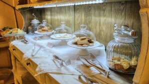 Un buffet con diversi cibi esposti in contenitori di vetro e piatti da portata, posate disposte su un tavolo e uno sfondo in legno.