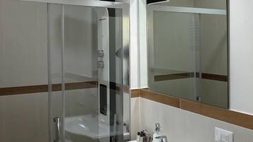 A bathroom with a glass shower enclosure, a white sink with a mirror above it, and a towel rack.