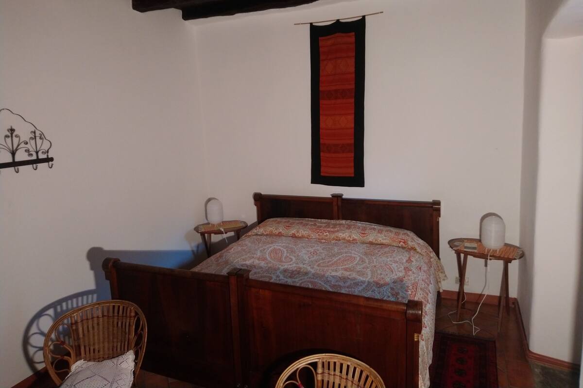 A bedroom with a wooden bed, two bedside tables, a chair, and a wall-mounted red tapestry.