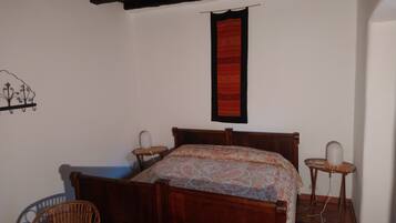 A bedroom with a wooden bed, two bedside tables, a chair, and a wall-mounted red tapestry.