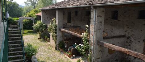 A rustic stone building with a sloped roof, a staircase leading to a covered area, and potted plants around the exterior.