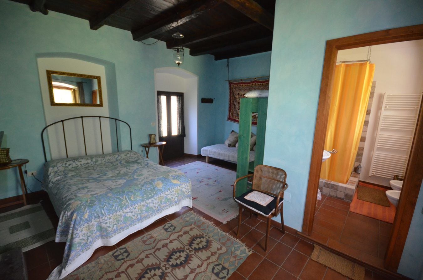 A bedroom with a bed, a chair, a window, and a door leading to a bathroom.