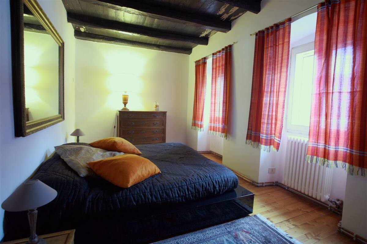 A bedroom with a bed, dresser, lamp, and curtains.