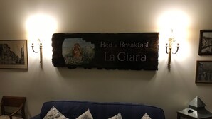A room with a dark blue sofa, floral-patterned cushions, a wall-mounted sign reading "Bed & Breakfast La Giara," and two wall sconces with candles. - La Giara Rooms (Verona)