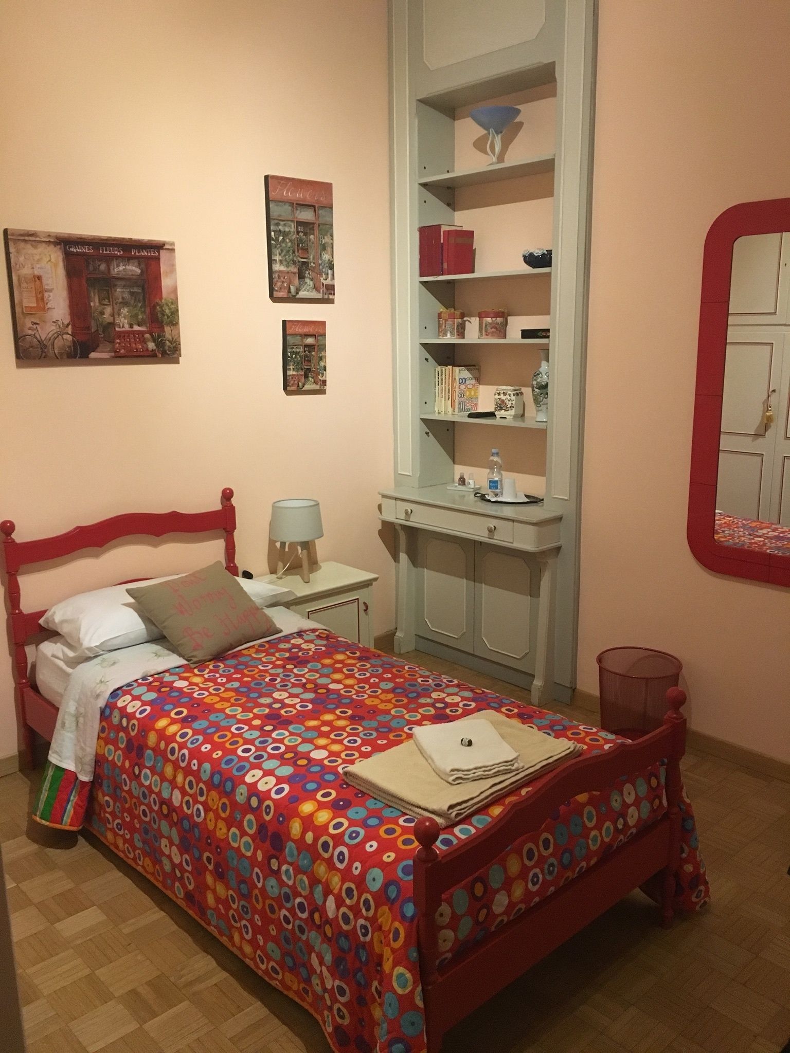 Ein Schlafzimmer mit einem roten Bett, einem Schreibtisch mit Lampe und einem Regal mit Büchern und Dekoration.
