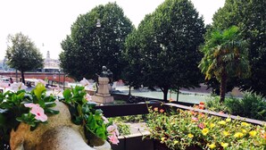 A view of a river with a statue in the background, surrounded by trees and a flower bed in the foreground. - La Giara Rooms (Verona)
