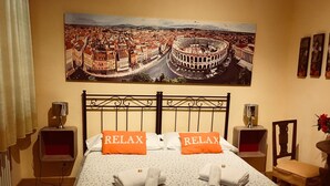 A hotel room with a bed, two pillows with 'RELAX' text, a painting of a cityscape, and a small table with a chair. - La Giara Rooms (Verona)