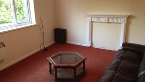 A living room with a glass-top coffee table, a dark leather sofa, a fireplace, and a window with a view of trees. - Ranmoor Lodge (Sheffield)