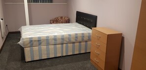 Une chambre à coucher avec un lit, une commode, un radiateur et une fenêtre avec des barreaux.