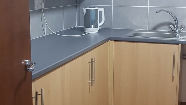 A kitchen with wooden cabinets, a sink, and a kettle on the countertop. - Ranmoor Lodge (Sheffield)