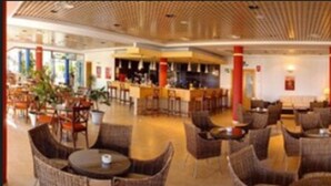 A spacious indoor area with multiple seating arrangements, including round tables and chairs, and a bar area with stools. - Hotel Punta del Cantal  (Mojacar)