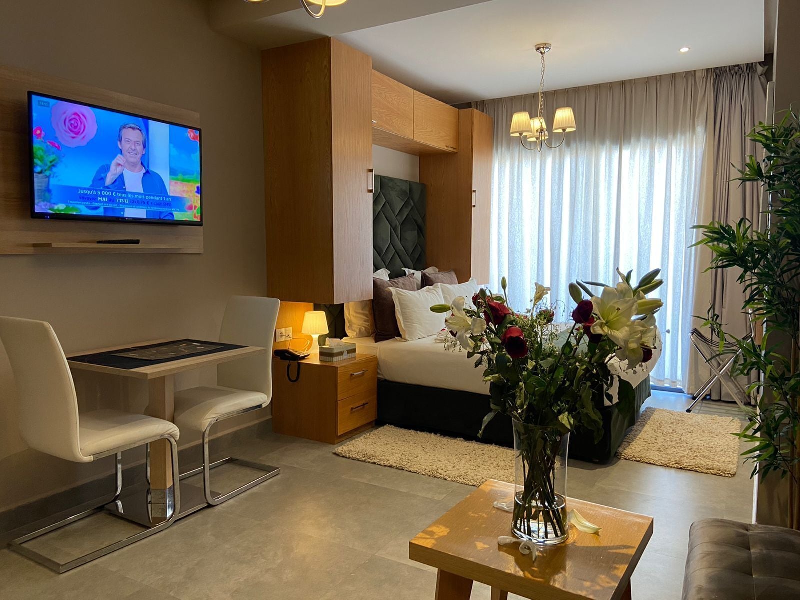 Une chambre d’hôtel moderne équipée d’un lit, d’un bureau, d’une télévision et d’un vase de fleurs.