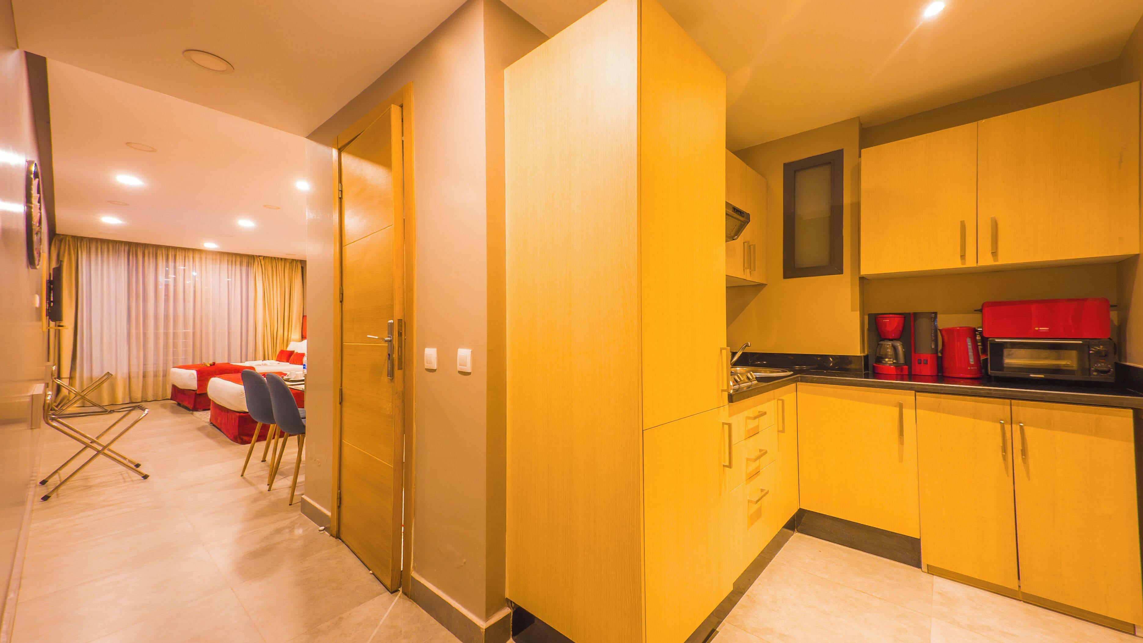 Habitación de hotel con kitchenette, cama con ropa de cama roja y televisión montada en la pared.