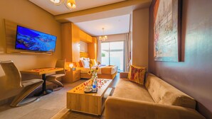 A modern hotel room with a large TV, a sofa, a coffee table with rose petals, and a view of the outdoors.