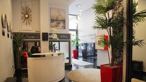 A modern reception area with a white reception desk, a large potted plant, and a red accent chair.
