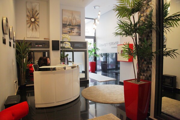 A modern reception area with a white reception desk, a large potted plant, and a red accent chair. - Dayet Ifrah by Rent Inn (Rabat)