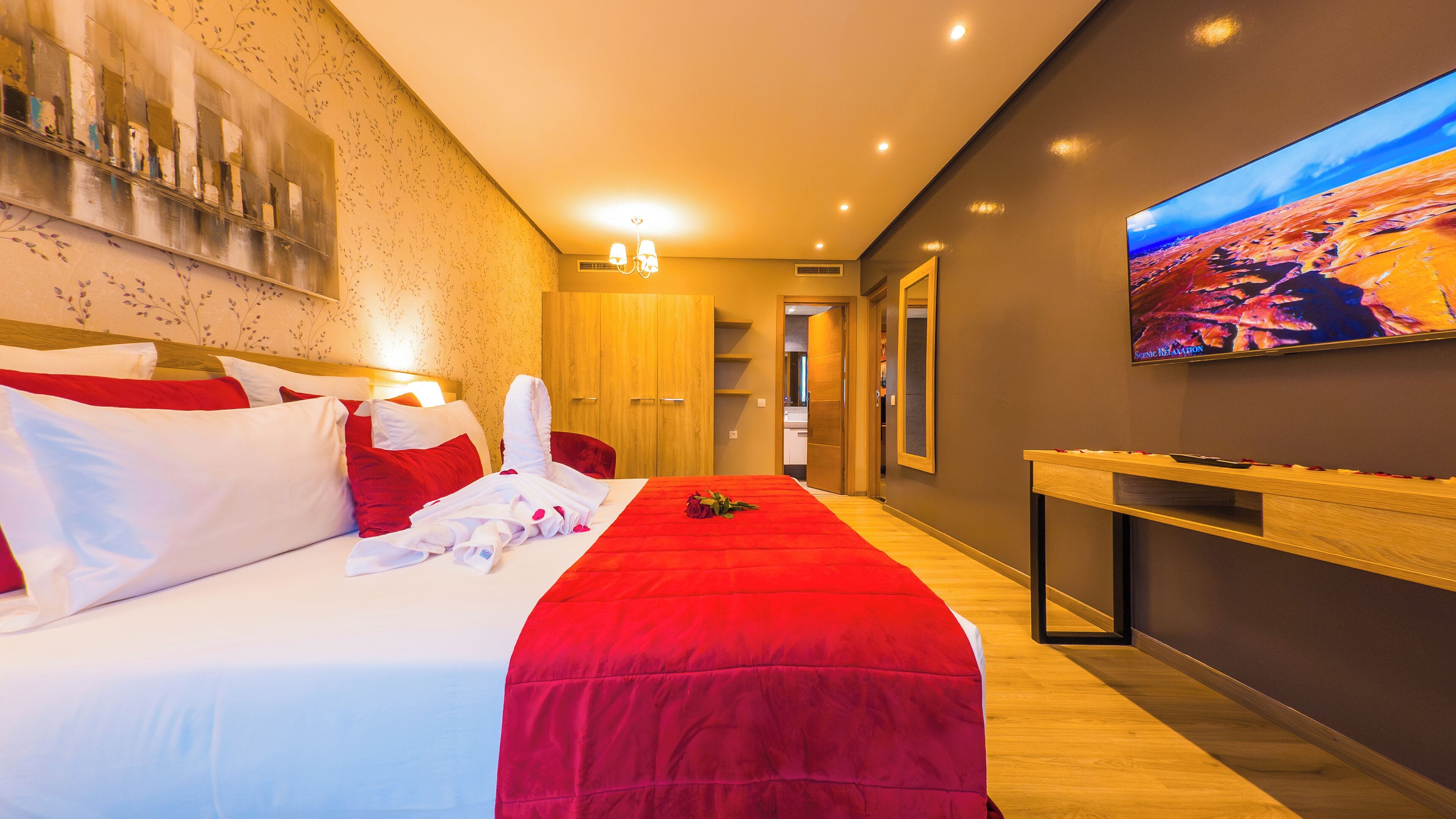 Una habitación de hotel con una cama grande, un televisor en la pared y un aparador de madera.