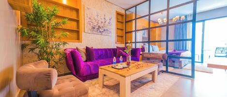 A modern living room with a purple sofa, a wooden coffee table, and a large window.