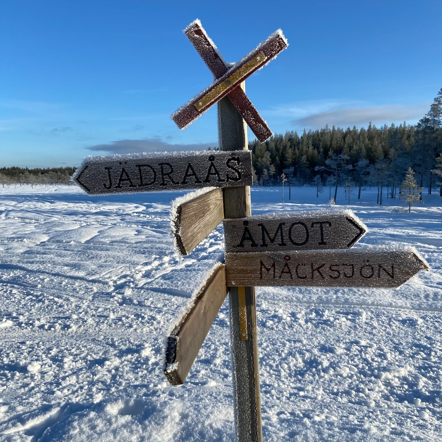 Een houten wegwijzer in een besneeuwd landschap met heldere lucht.