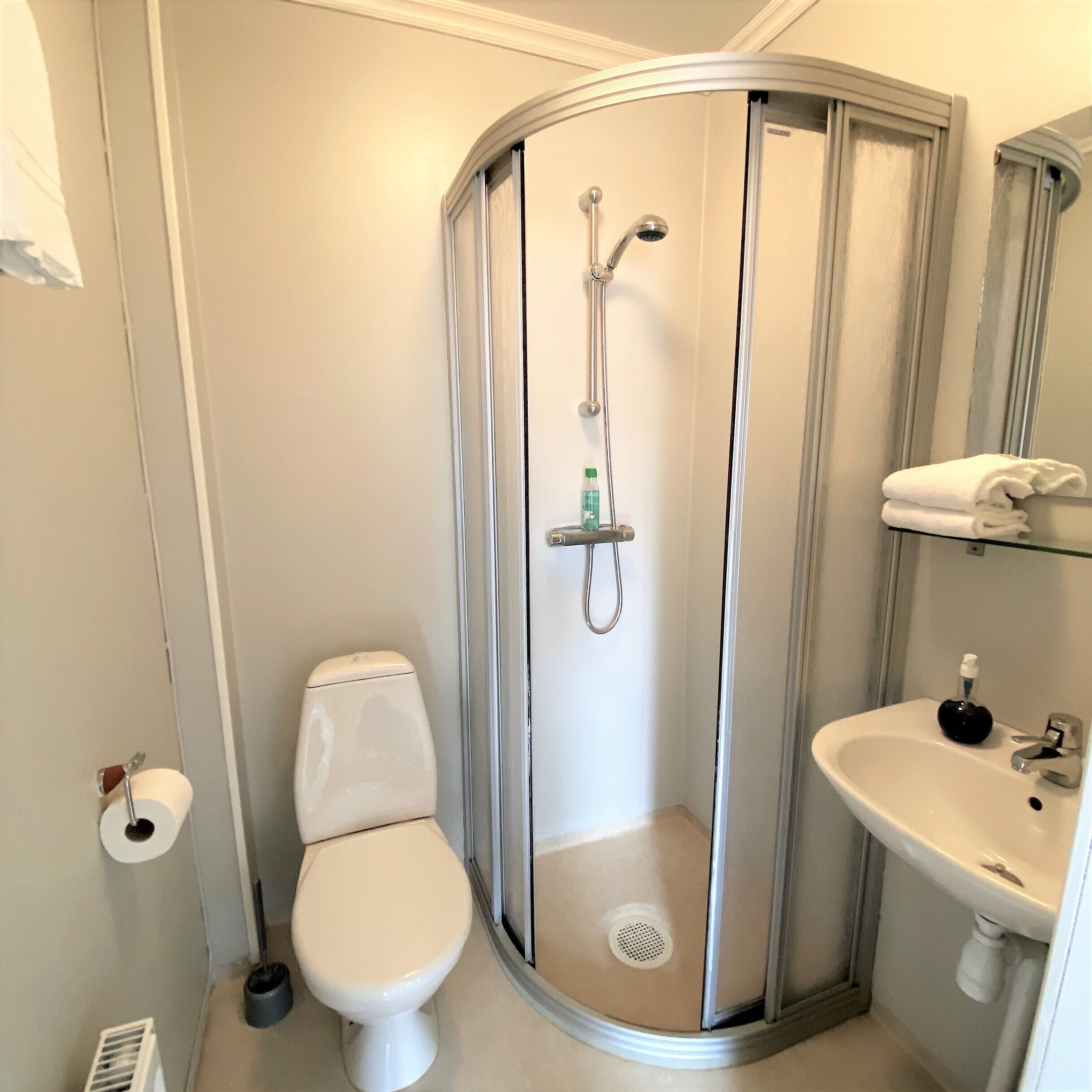 Un baño compacto con inodoro, cabina de ducha con mampara de vidrio y lavamanos con dispensador de jabón.