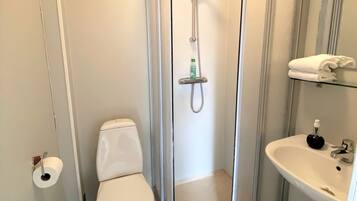 Un baño compacto con inodoro, cabina de ducha con mampara de vidrio y lavamanos con dispensador de jabón.