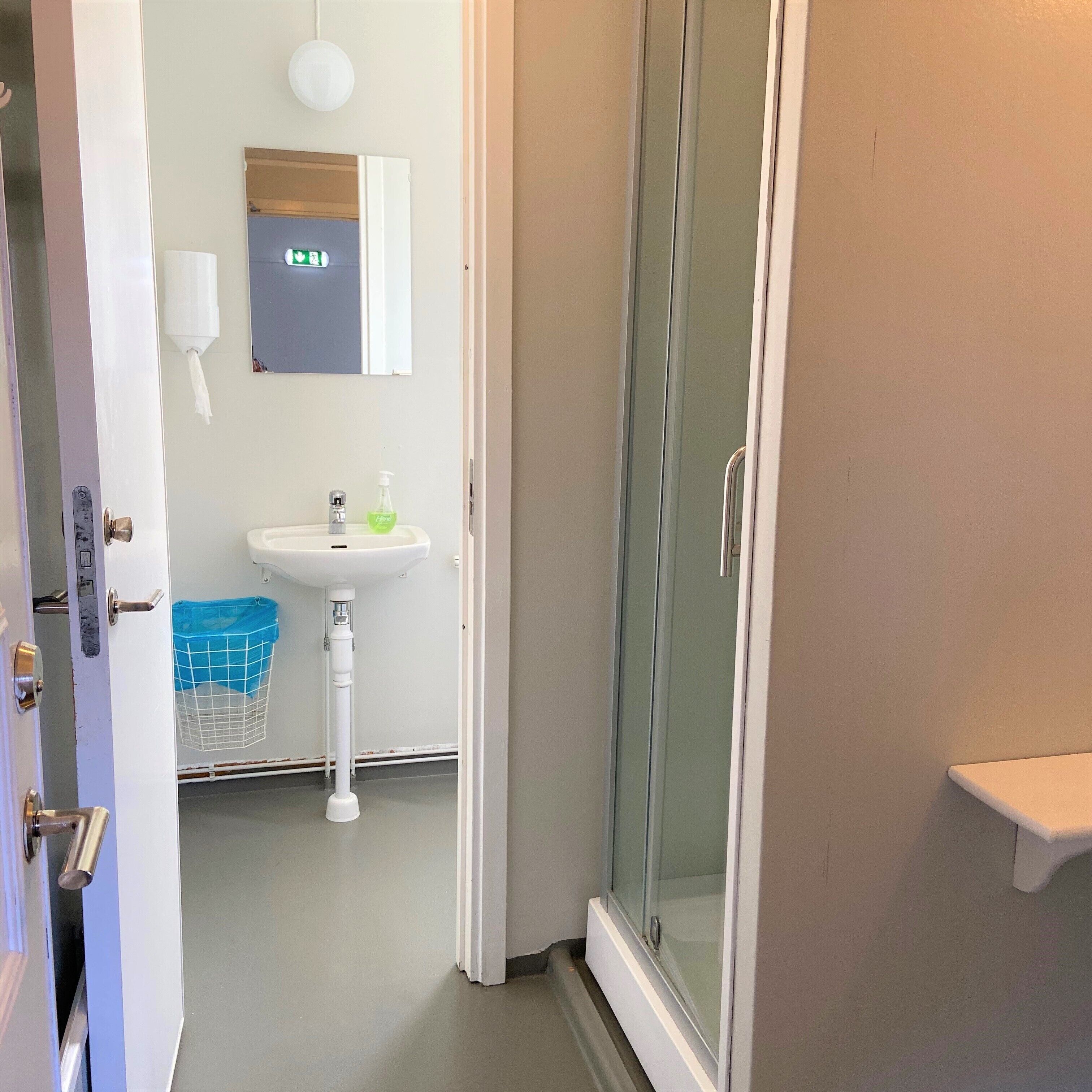 A bathroom with a glass shower door, a sink with a soap dispenser, and a towel rack.