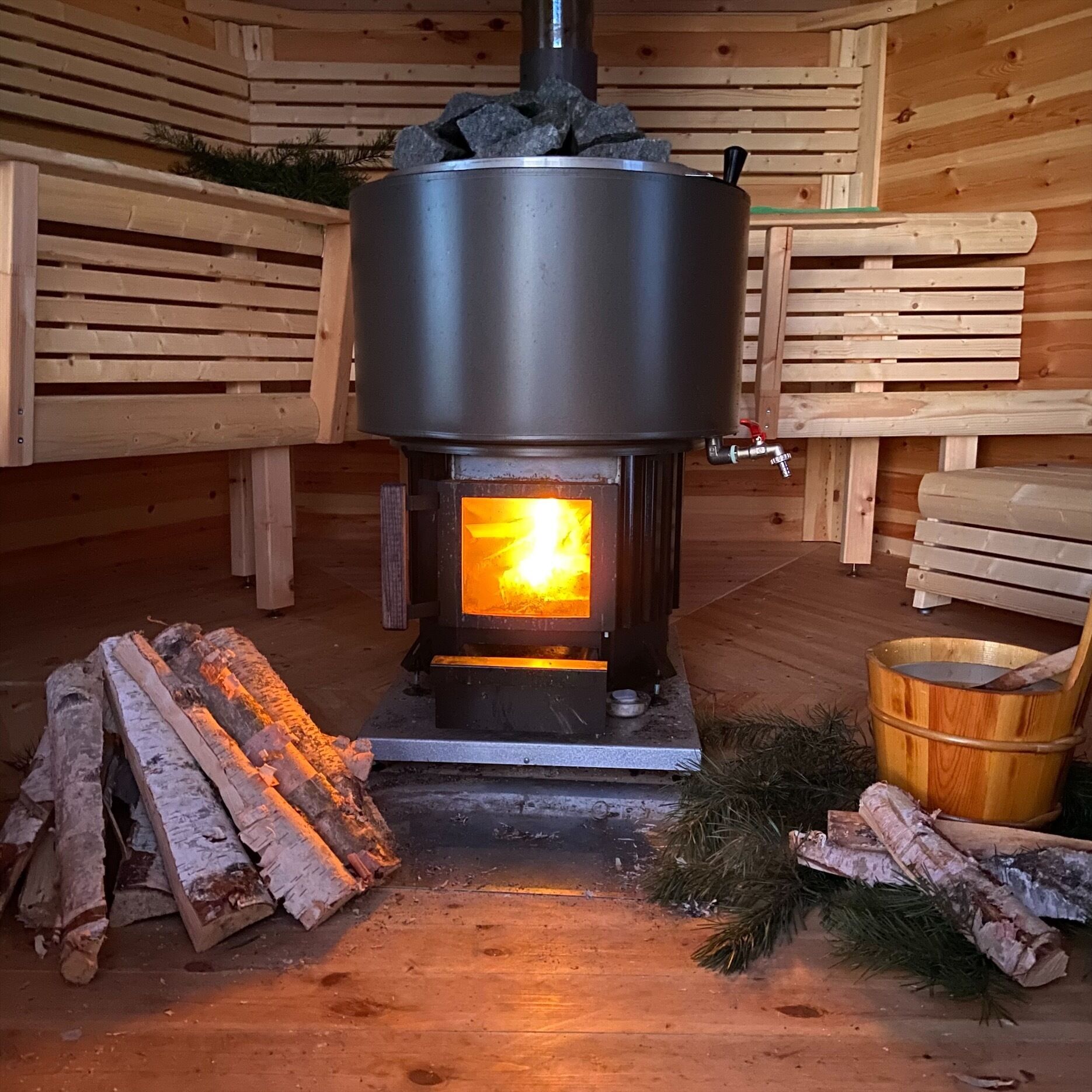 A wood-burning stove with logs and a bucket of water nearby.