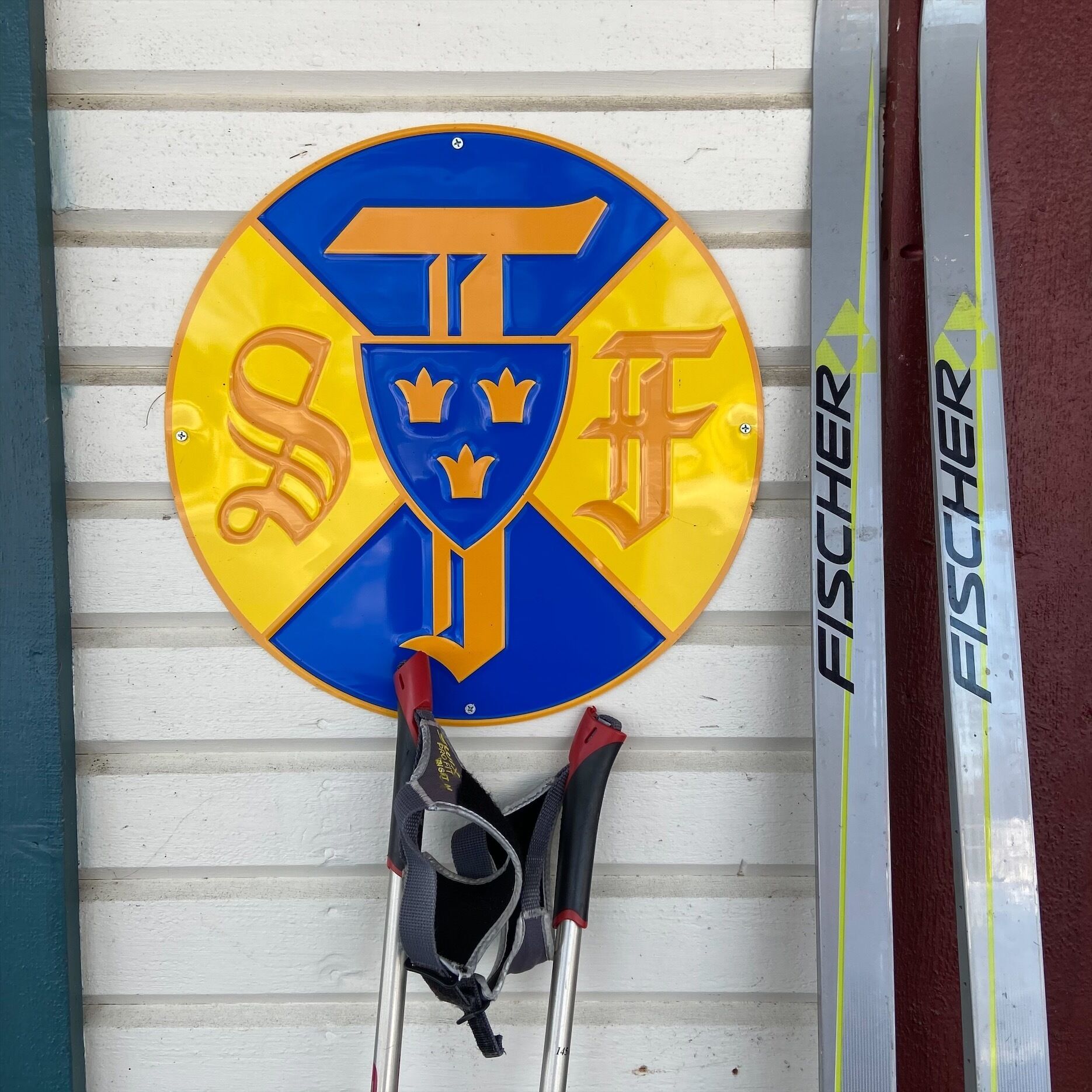 Een rond bord met een blauw en geel symbool met de letters 'STF' en een kroon, bevestigd aan een witte muur.