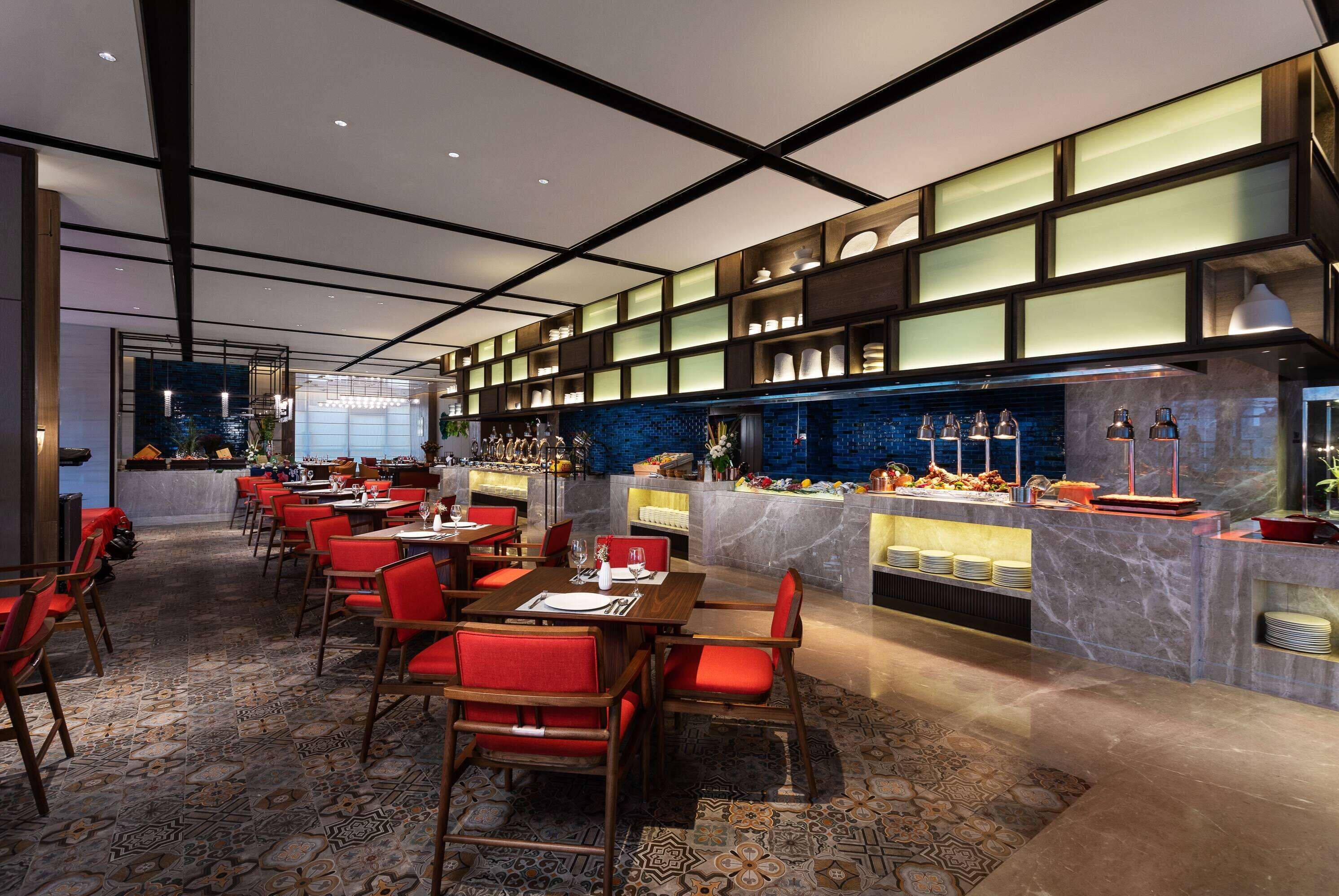 A modern restaurant with a long counter, red chairs, and a blue-tiled backsplash.