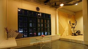 A room with a large window, a small round table with a vase, and a wall-mounted exercise bike. - Busket Hostel (Chiang Rai)