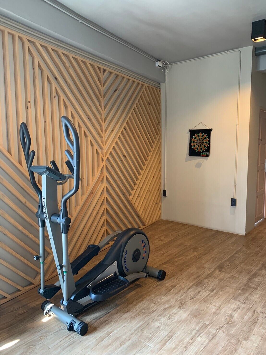 A room with a wooden herringbone wall pattern, a stationary bike, and a dartboard on the wall.