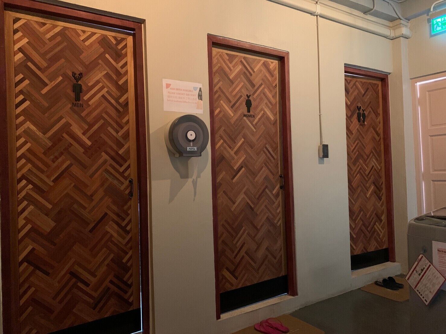 Een gang met drie houten deuren, elk aangeduid voor heren en dames. Een rookmelder is aan de muur tussen de deuren bevestigd.