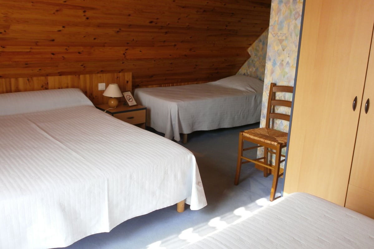 Quarto com duas camas, uma cadeira, mesa de cabeceira com abajur e guarda-roupa.