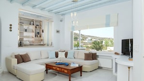 A modern living room with a sectional sofa, a wooden coffee table, and a TV on a white stand. - Tatiana Villa & Apartments (Mykonos)