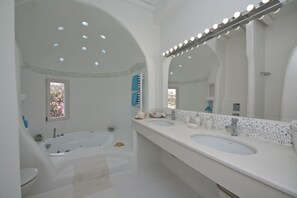 A modern bathroom with a large bathtub, two sinks, and a vanity mirror. - Tatiana Villa & Apartments (Mykonos)