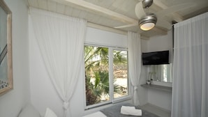 A hotel room with a bed, a TV, a window with curtains, and a ceiling fan. - Tatiana Villa & Apartments (Mykonos)
