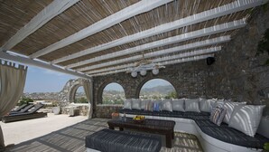 A covered outdoor seating area with stone walls, a sofa, and a table. - Tatiana Villa & Apartments (Mykonos)