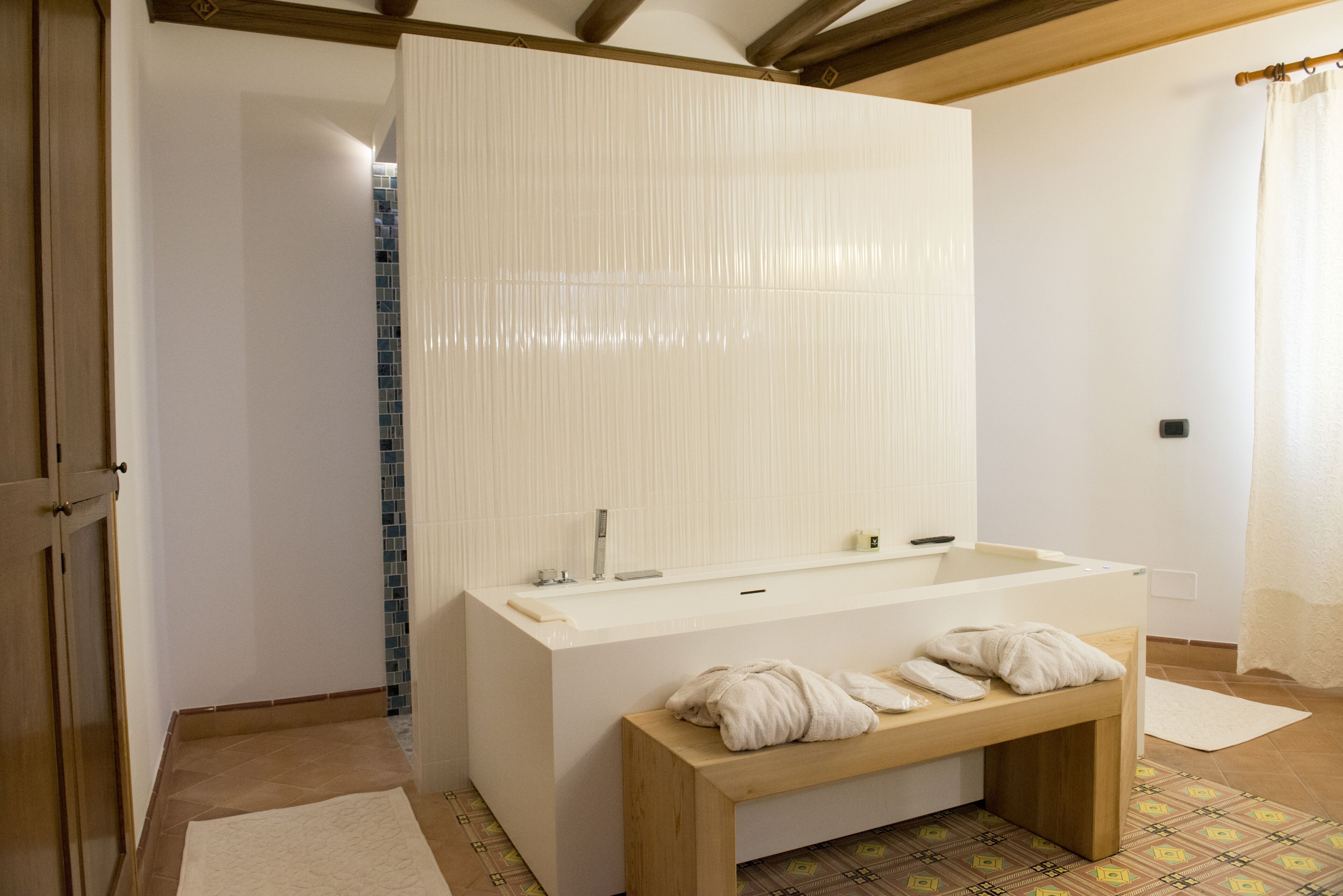 Ein modernes Badezimmer mit einer großen Badewanne, einer Holzbank und einem Fliesenboden.