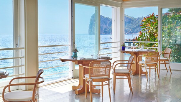 A dining area with a view of the sea, wooden furniture, and a table with a vase and glasses. - Taverna del Capitano (Massa Lubrense)