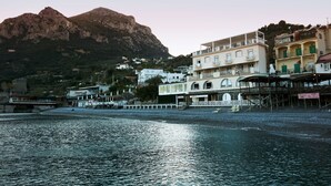 A coastal town with buildings along the waterfront, a mountain in the background, and a bridge crossing the water. - Taverna del Capitano (Massa Lubrense)