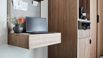 A modern kitchen with a built-in laptop on a wooden counter, a vase with flowers, and a coffee machine.