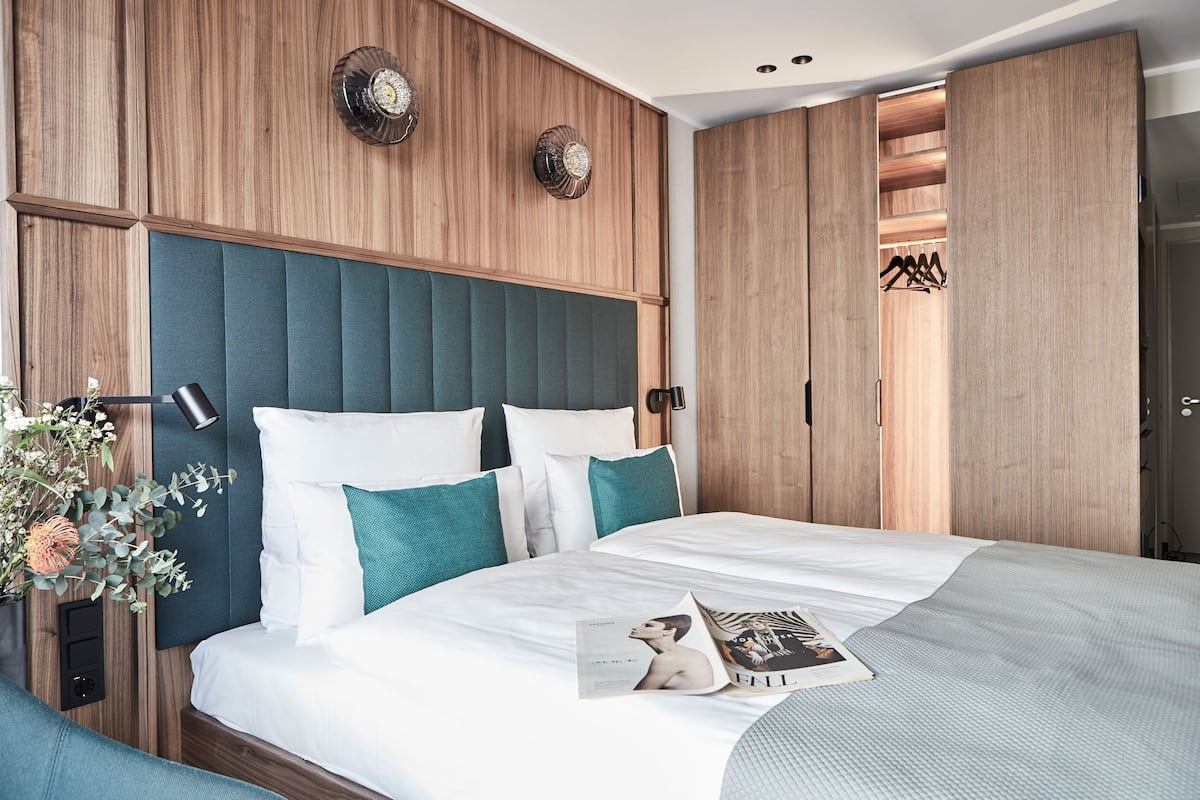 Une chambre à coucher moderne avec une tête de lit en bois, un lit avec une literie blanche et turquoise, et un magazine posé sur le lit.