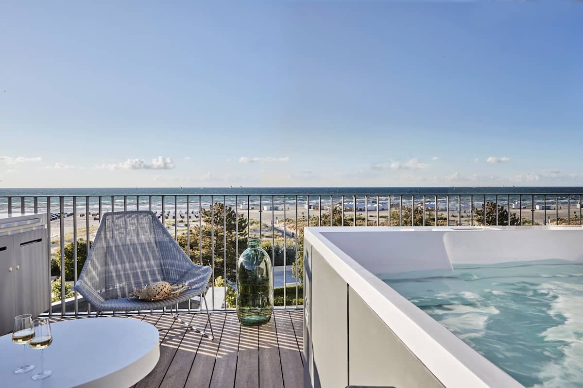 Un balcon avec vue sur la plage, un jacuzzi et un coin salon avec une table en verre et deux verres.