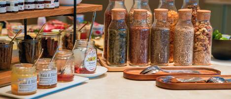 Una mesa de buffet con diferentes alimentos y condimentos, incluyendo frascos de conservas y botellas de salsas.