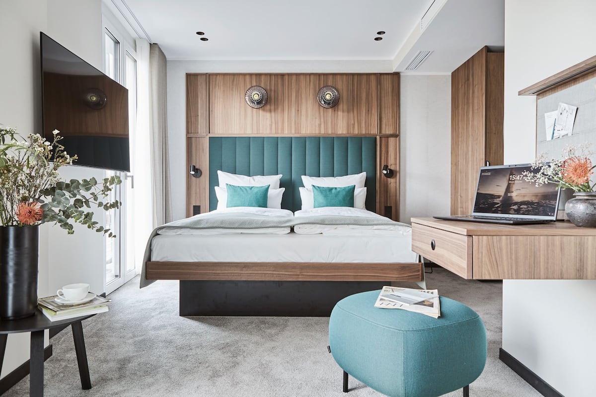 Une chambre d’hôtel moderne dotée d’un grand lit, d’un bureau avec un ordinateur portable, d’un petit coin salon et d’une grande fenêtre.